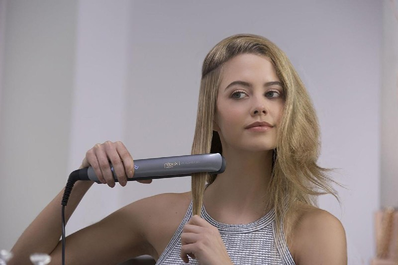 Mujer usando una plancha para el pelo. Tiene cabello rubio. Espejo en el fondo.