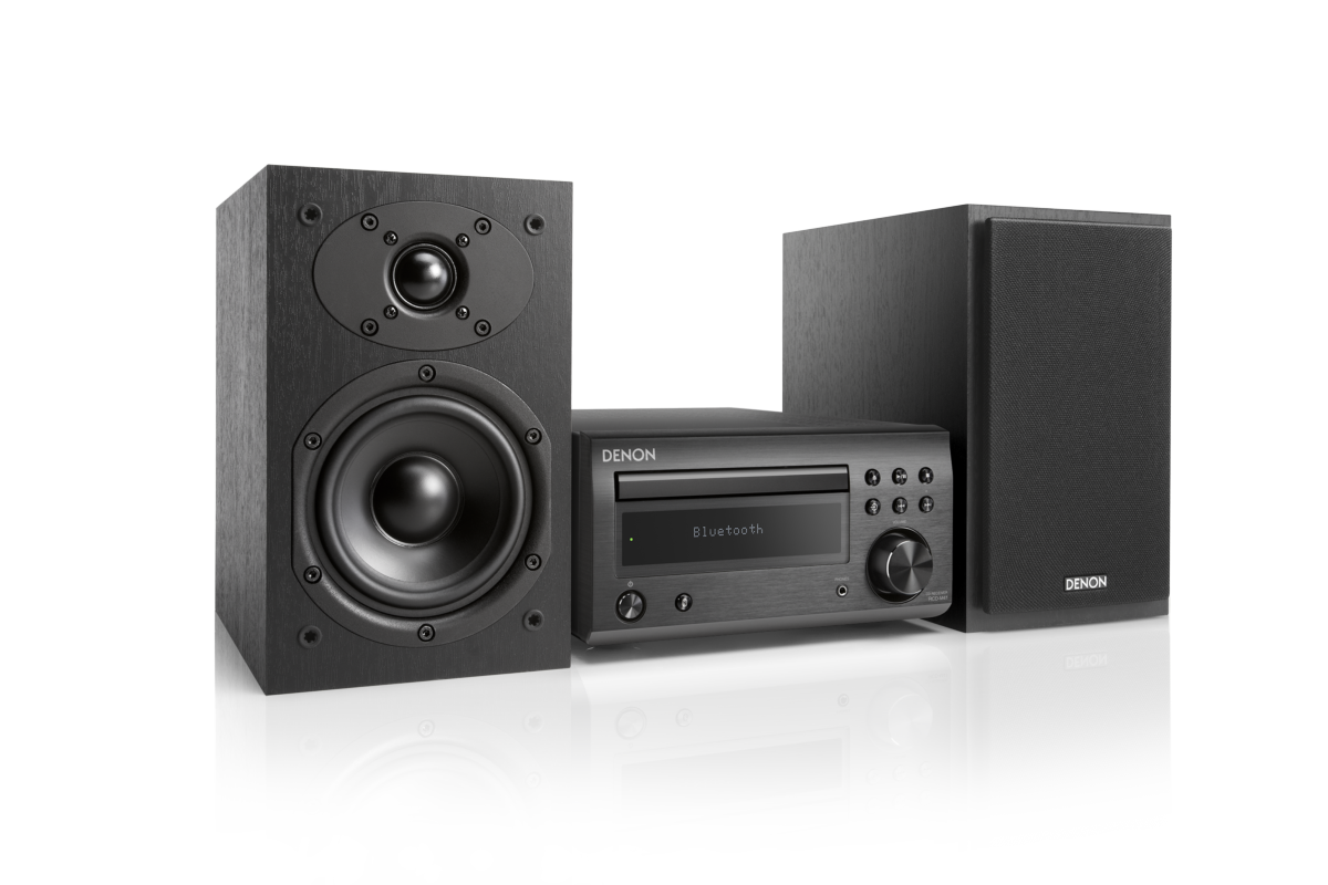 Un sistema de audio Denon negro con dos altavoces. El sistema está sobre una superficie blanca reflectante.