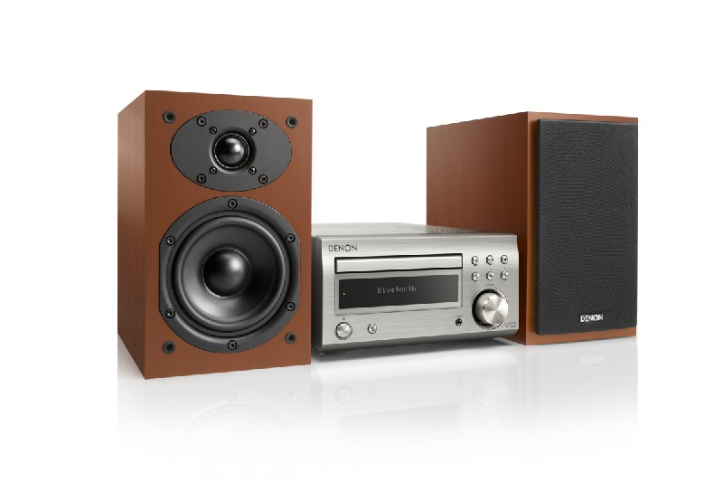 Un sistema de audio Denon con reproductor de CD, dos altavoces y acabado plateado, sobre fondo blanco.