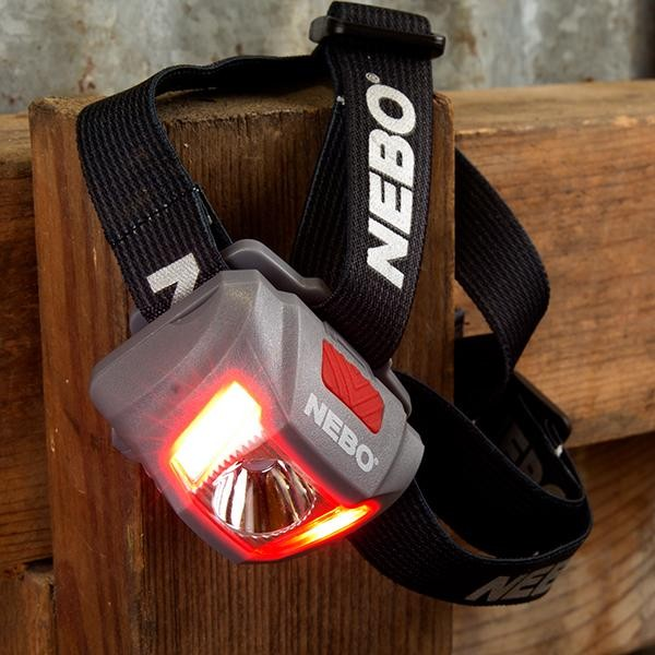 Linterna frontal gris con luz roja sobre madera. Correa negra con texto "NEBO".