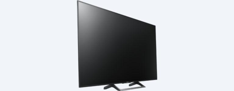 Un televisor de pantalla plana negro grande sobre un soporte. La pantalla está apagada, mostrando un reflejo.