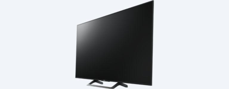 Un televisor de pantalla plana negro grande, en ángulo hacia un lado, con un soporte sobre un fondo blanco.