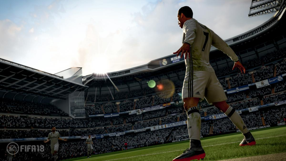 Futbolista en uniforme blanco celebra en estadio con público, logo FIFA 18 visible.