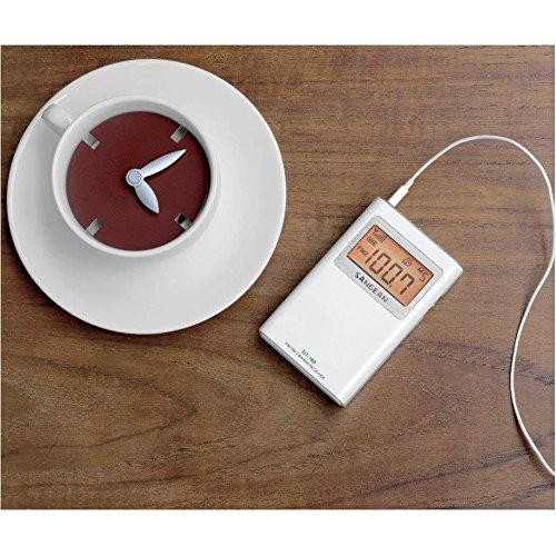 Taza blanca con sustancia similar al café. Un dispositivo digital con pantalla al lado.