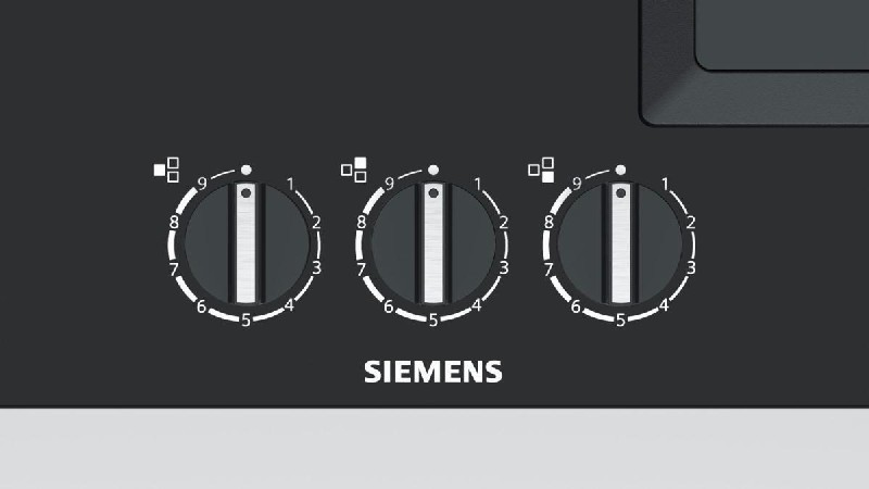 Primer plano de perillas de estufa Siemens con números, sobre una superficie negra.