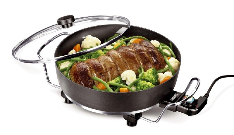 Olla negra redonda con comida. Verduras y carne dentro, tapa de vidrio arriba. Marca Princess.