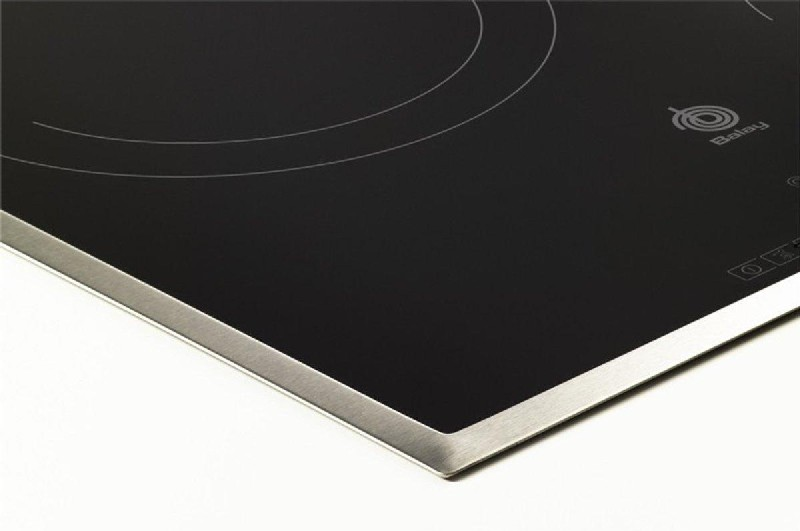 Primer plano de una esquina de placa de inducción negra. Borde de acero inoxidable, superficie negra, fondo blanco.