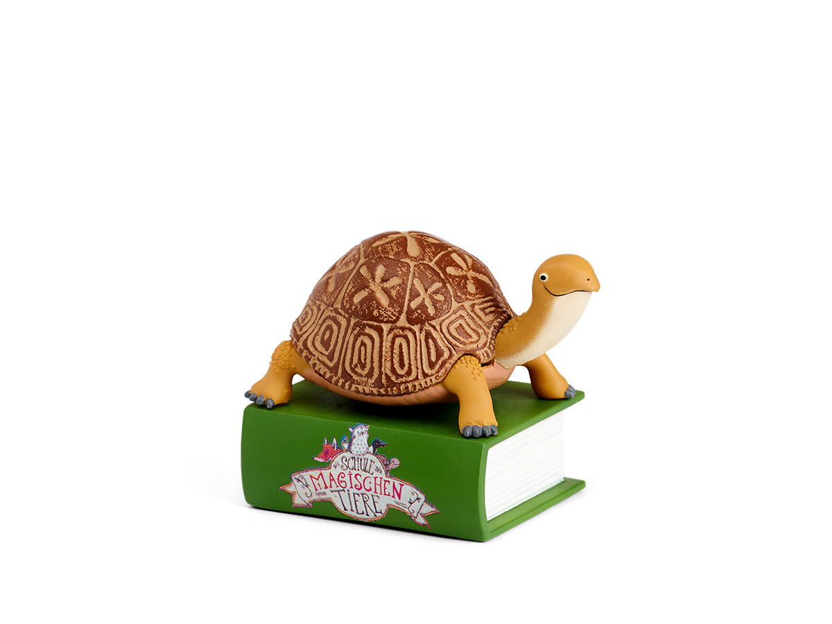 Eine Spielzeugschildkröte sitzt auf einem grünen Buch mit dem Titel „Die magischen Tiere“. Der Hintergrund ist weiß.