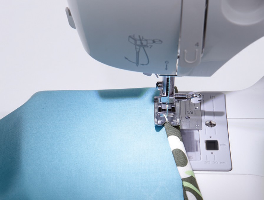 Máquina de coser en acción, cosiendo tela azul al borde de una tela estampada.