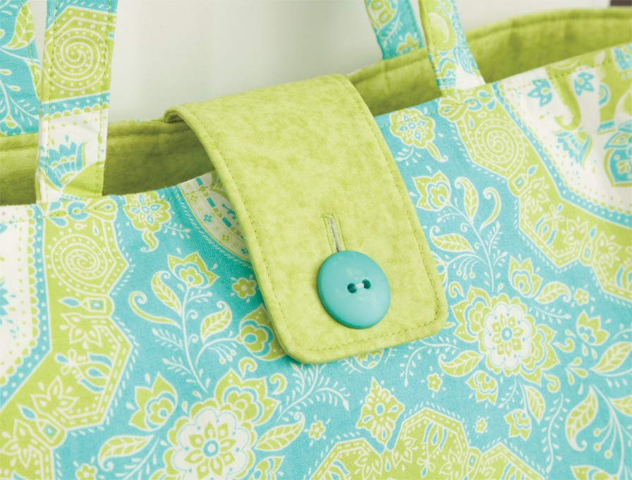 Primer plano de un bolso tote con estampado verde y azul con cierre de botón verde.