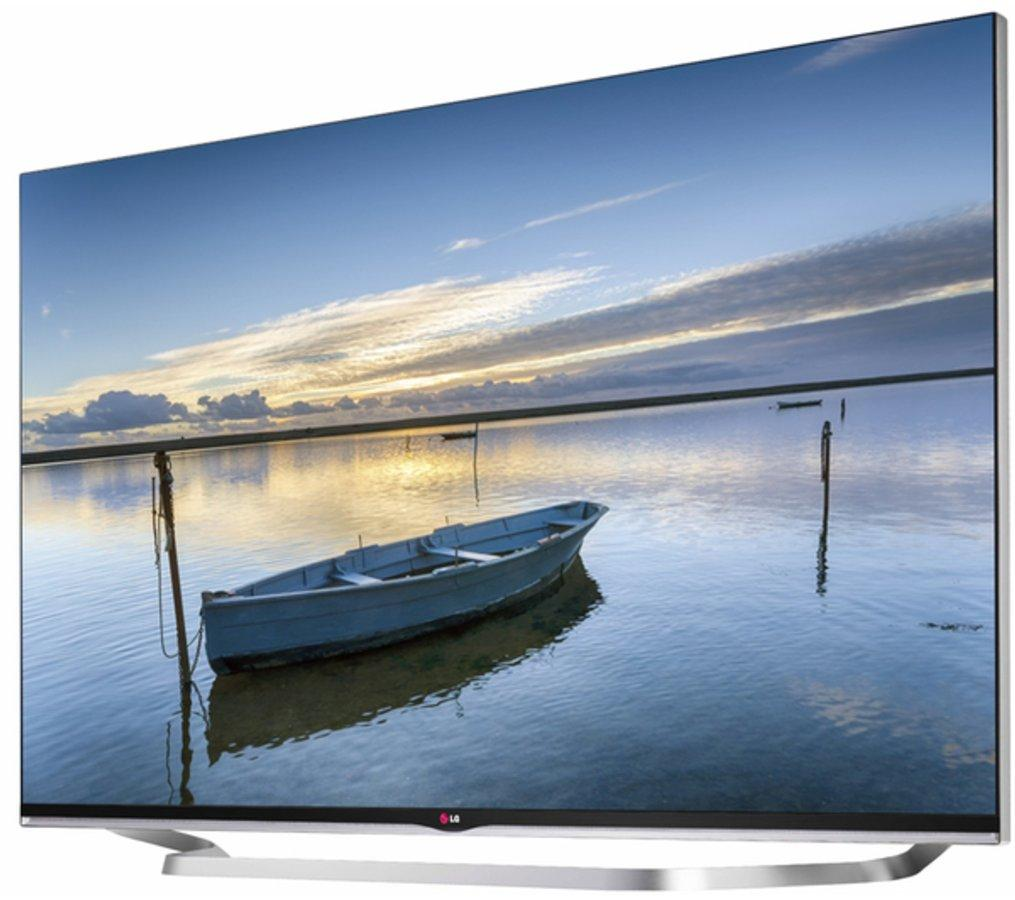 Televisor LG que muestra un barco en el agua con vista de puesta de sol. El televisor tiene soporte plateado y marco delgado.