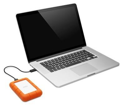 Portátil plateado conectado a un disco duro externo naranja por un cable negro.
