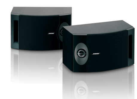 Dos altavoces Bose negros sobre una superficie blanca, con reflejo.