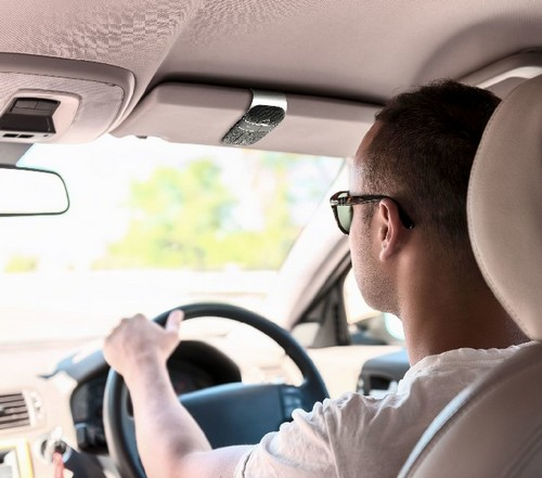 Un hombre conduciendo un coche, visto desde atrás. Usa gafas de sol y conduce con las manos en el volante.
