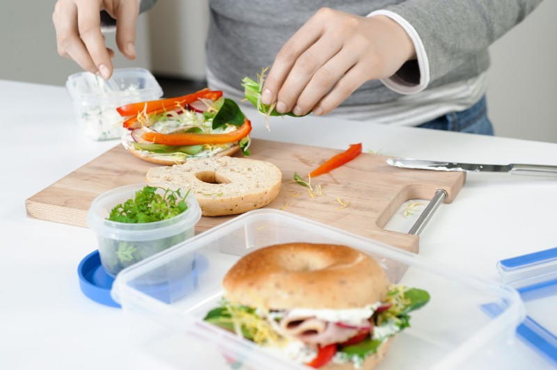 Manos preparando un sándwich de bagel con ingredientes frescos.
