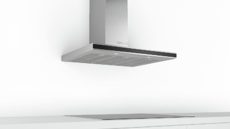 Una campana extractora de acero inoxidable montada en una pared blanca sobre una encimera negra.