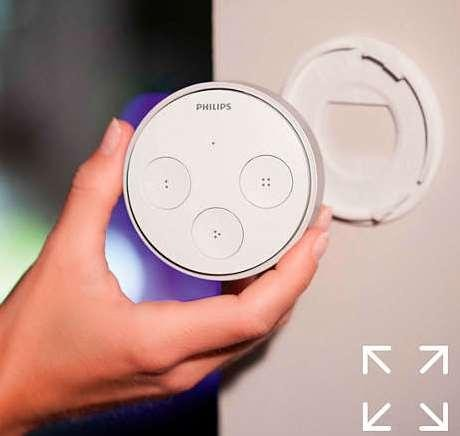Interruptor de atenuación Philips Hue blanco sostenido por una mano. Soporte de pared visible.