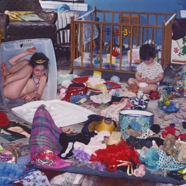 Unordentliches Zimmer mit zwei Kindern, eines in einer Kiste, das andere am Boden.