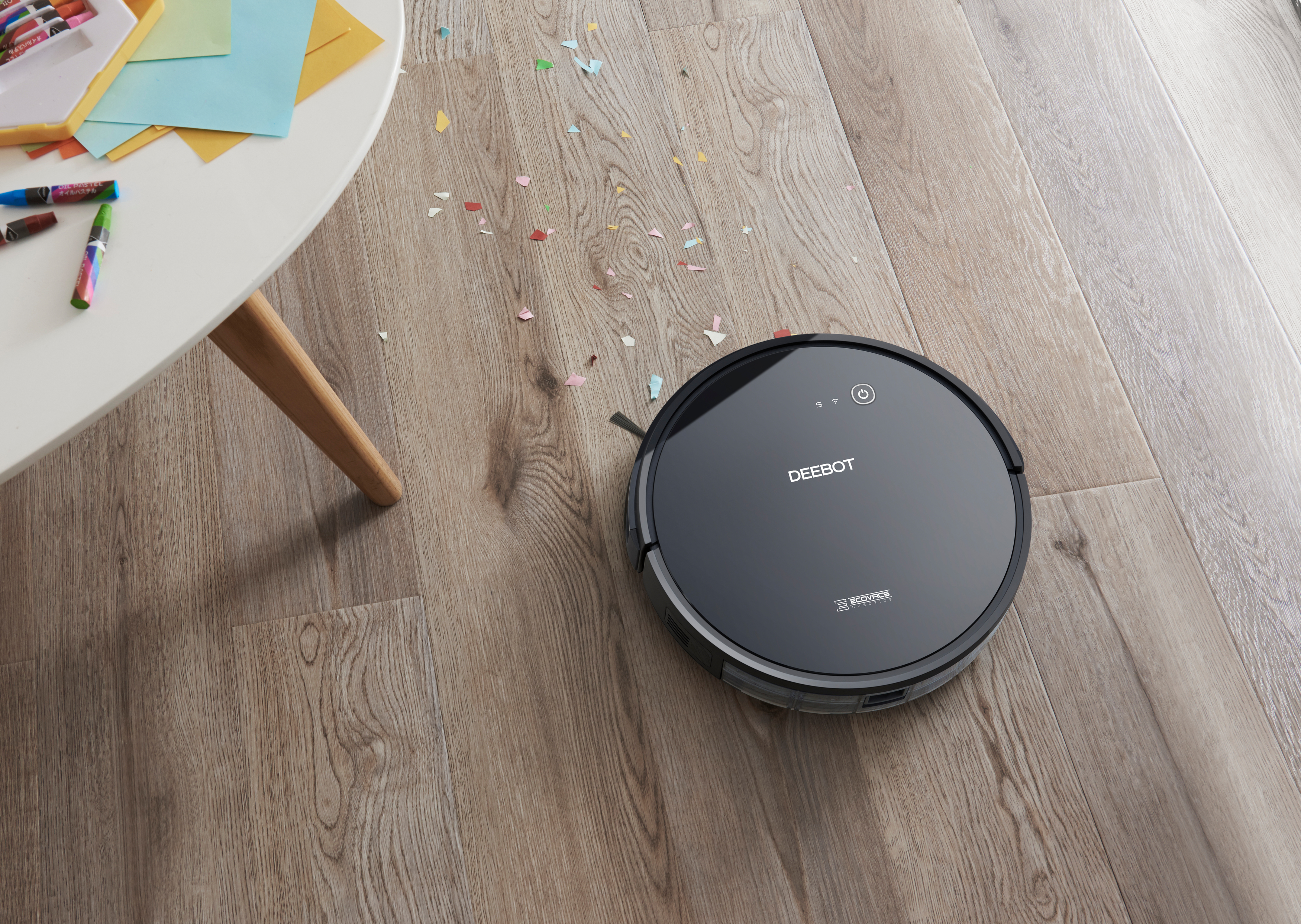 Schwarzer Roboter-Staubsauger auf Holzboden mit Konfetti in der Nähe.
