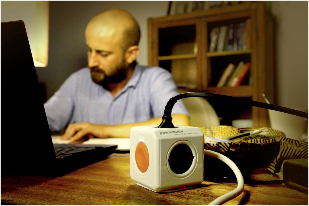 Fehér Powercube narancssárga díszítéssel, laptopba dugva, egy férfi a háttérben.