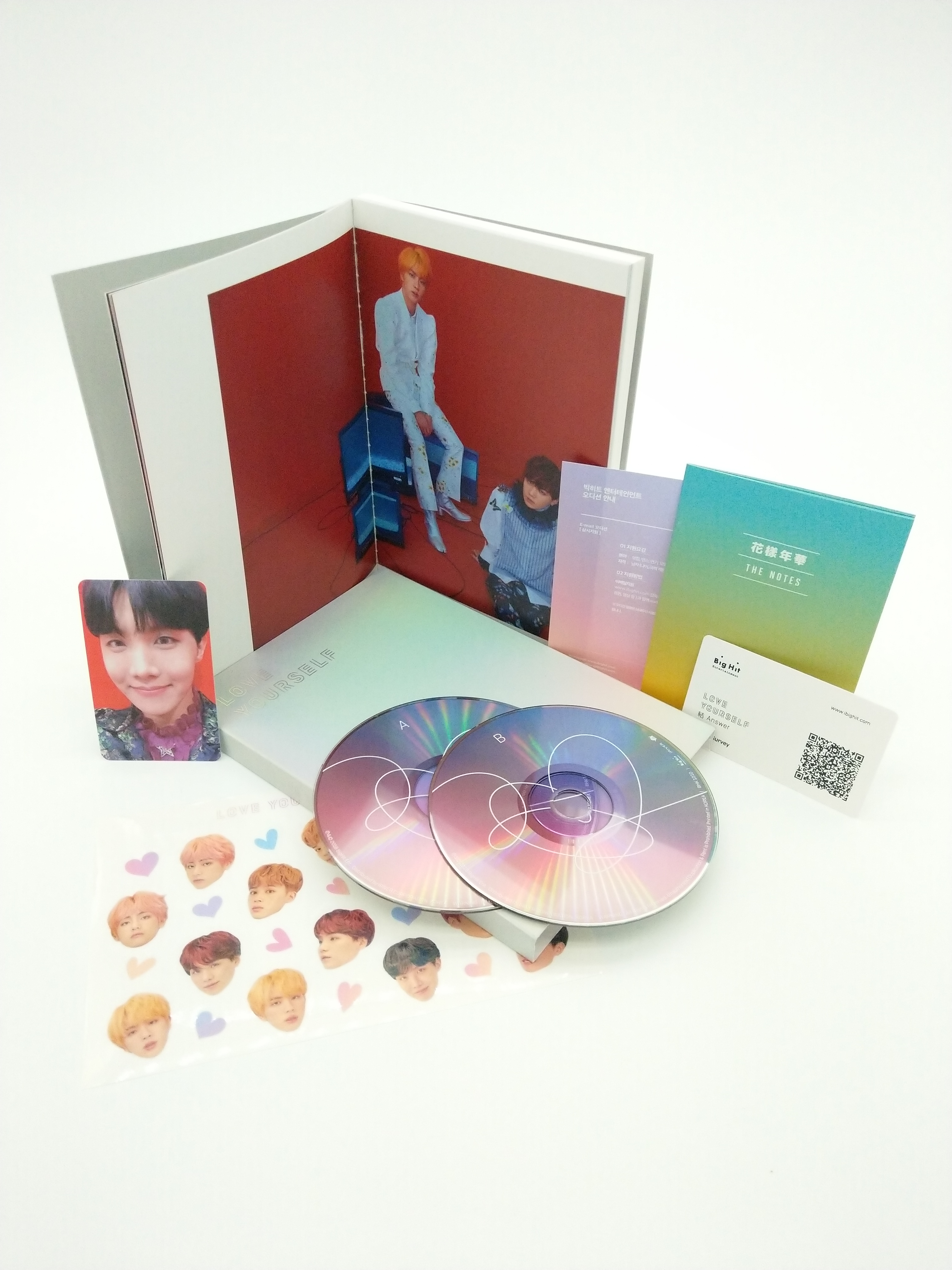BTS-Album-Set mit Alben, CDs, Fotokarten und Aufklebern. Die Artikel liegen auf einer weißen Oberfläche.