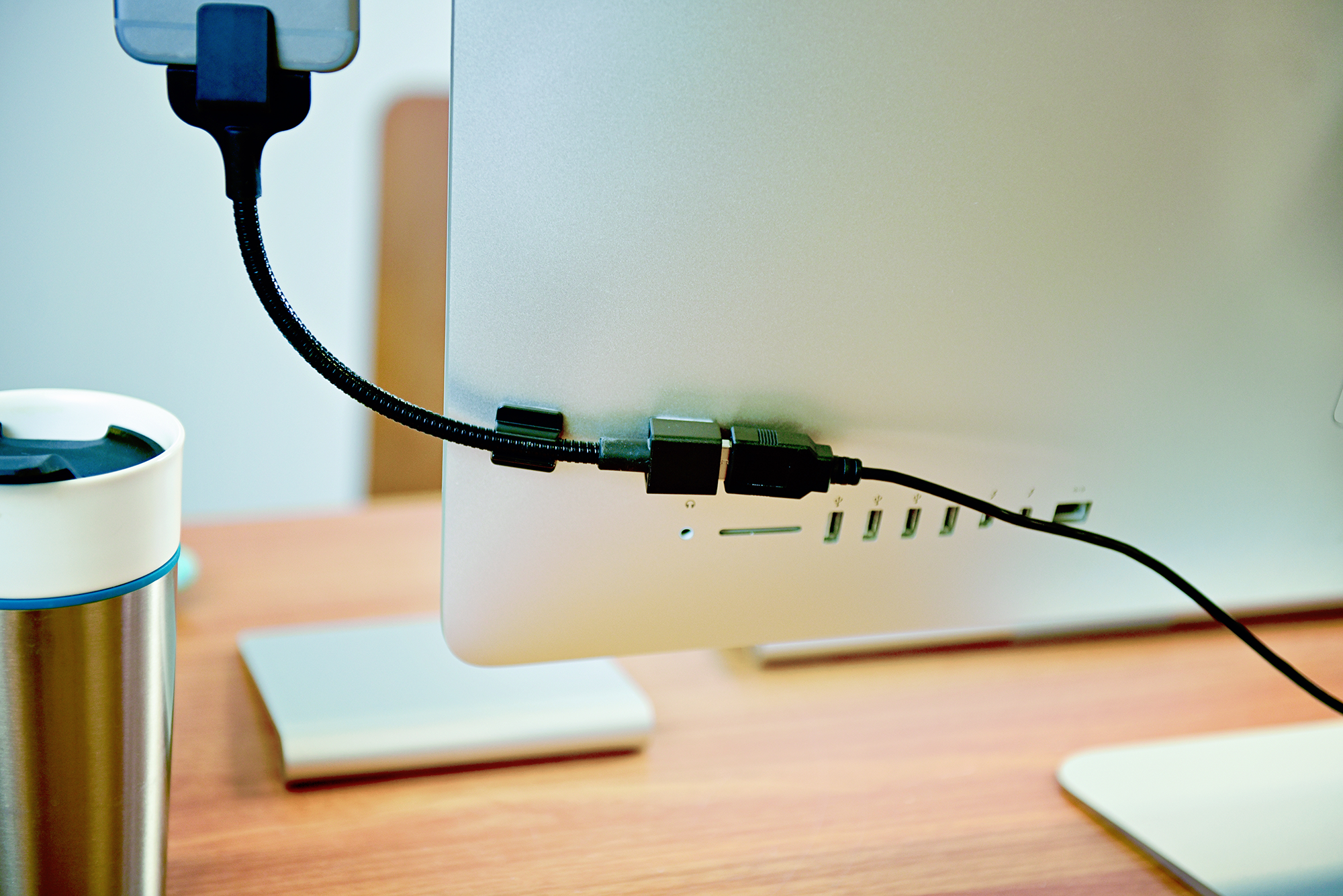 Achterkant computermonitor met aangesloten kabels. Een telefoon is bevestigd. Beker op de tafel.