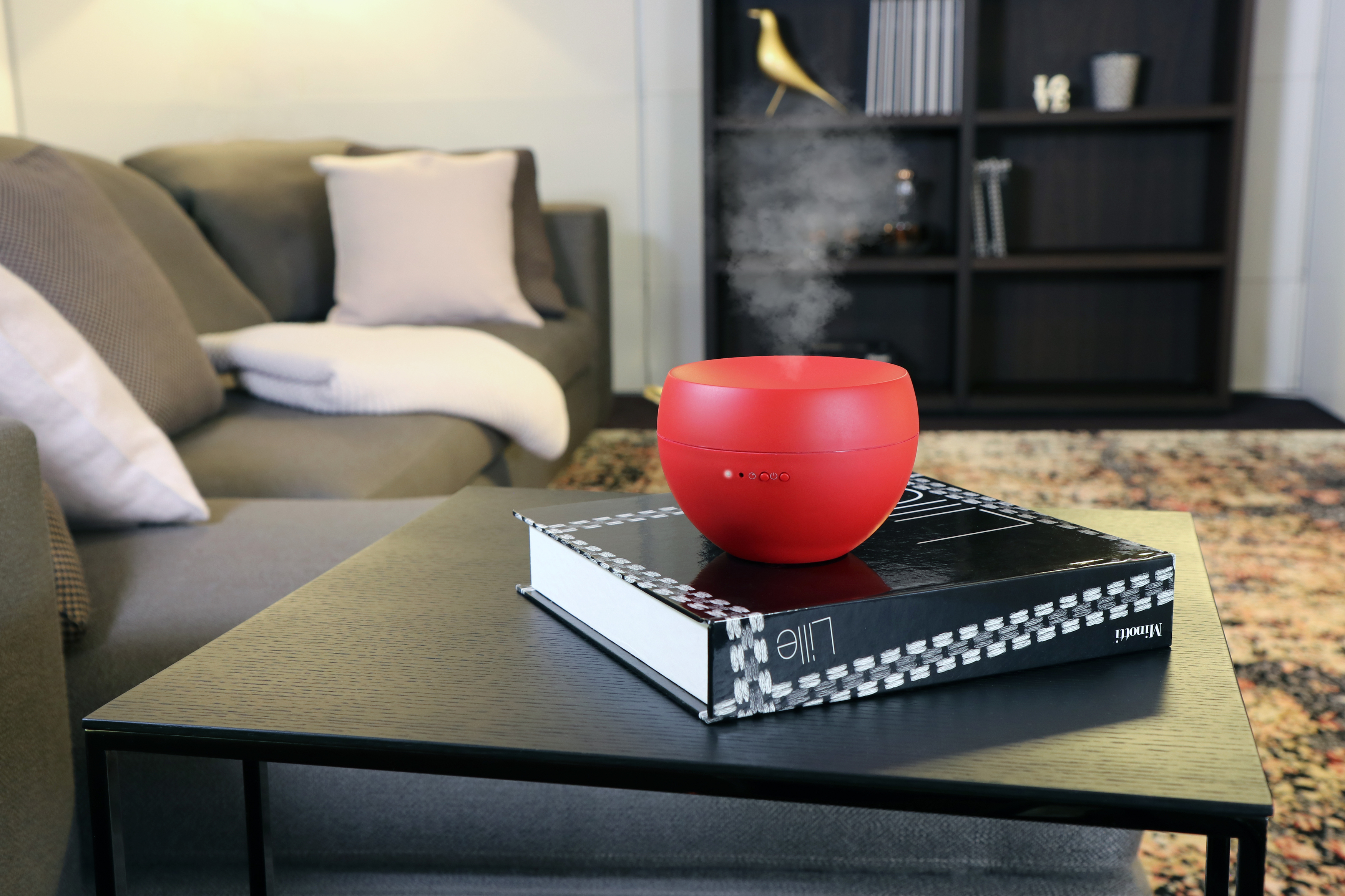 Roter Aroma-Diffusor auf einem schwarzen Tisch. Buch darunter, Sofa und Deko im Hintergrund.