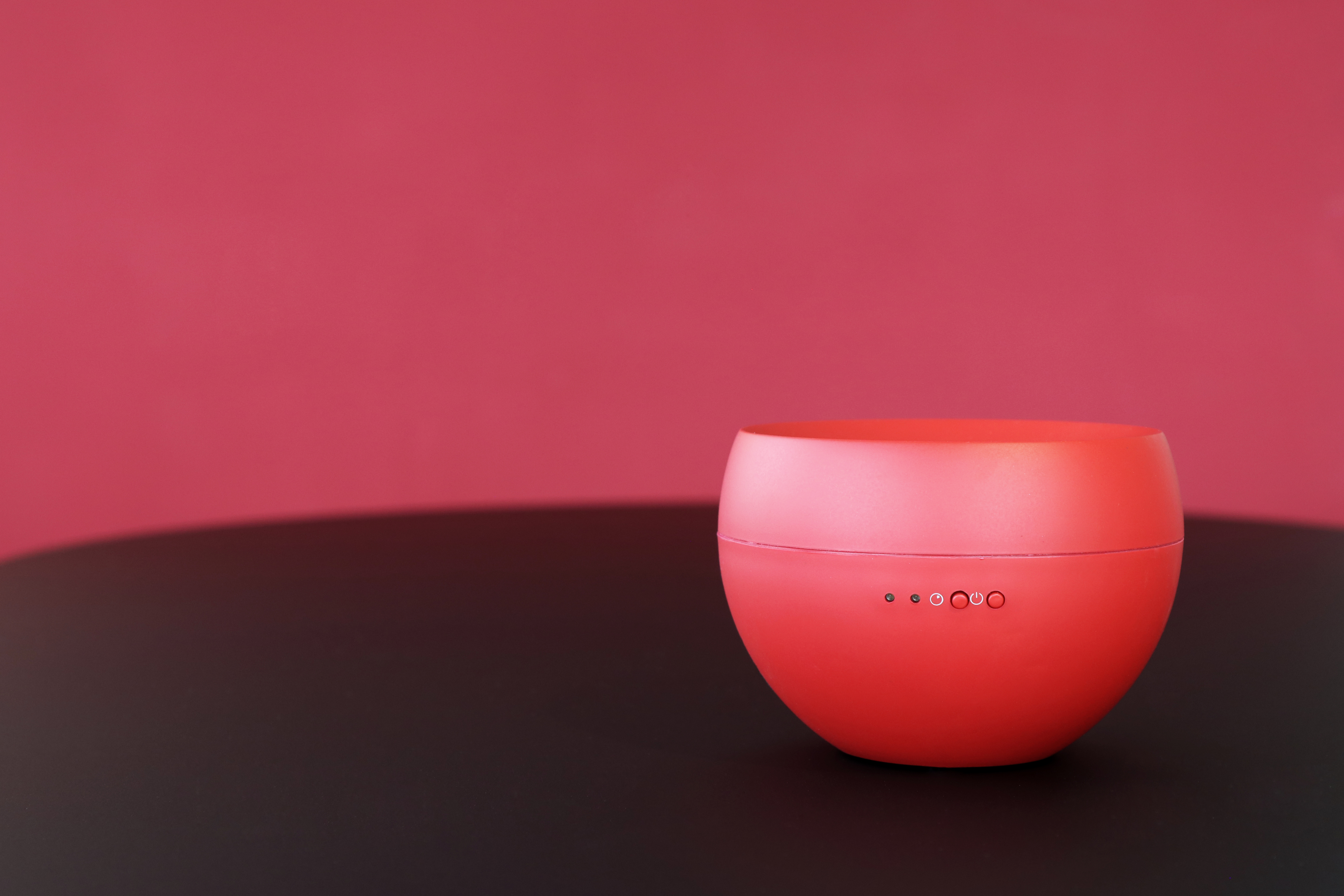 Roter, kugelförmiger Lautsprecher. Schwarze Tischoberfläche und rosa Hintergrund. Kleine Lichter am Lautsprecher.