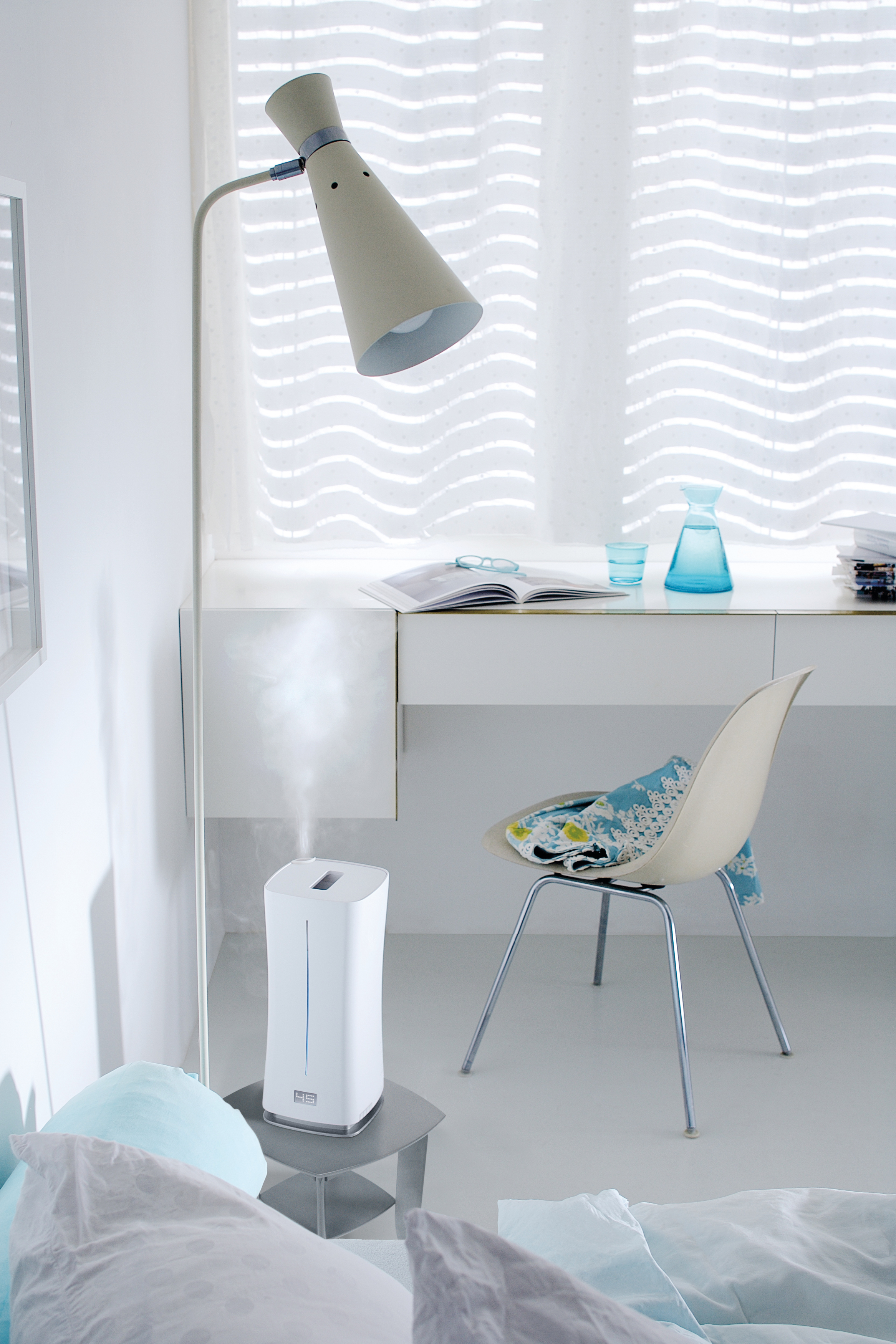 Modernes Zimmer mit Lampe, Schreibtisch, Stuhl und Luftbefeuchter. Weiße Wände und Boden.