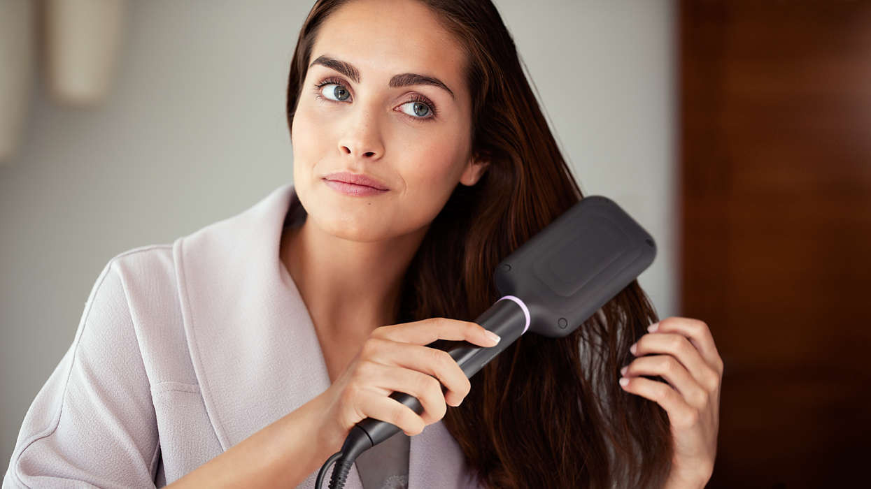 Vrouw die een haarstijlbürste gebruikt en naar de camera kijkt.