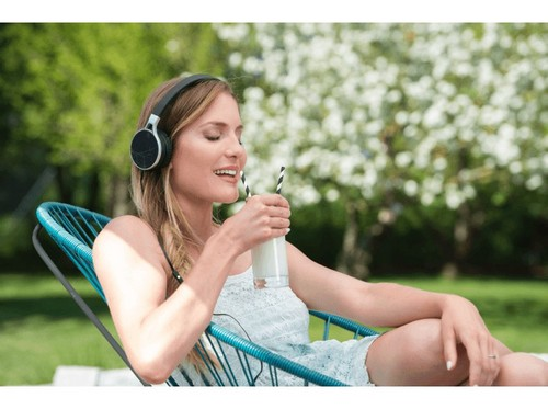 Mujer con auriculares bebiendo de un vaso con pajita. Fondo verde.