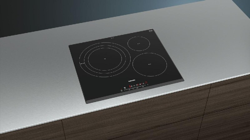 Placa de inducción negra integrada en una encimera. Tiene tres zonas de cocción. Fondo gris.