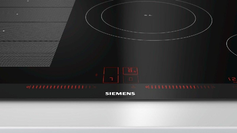 Placa de inducción Siemens negra. Controles táctiles con iluminación roja. Encimera blanca.
