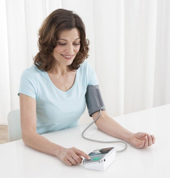 Una mujer tomándose la presión arterial con un monitor digital sobre una mesa.