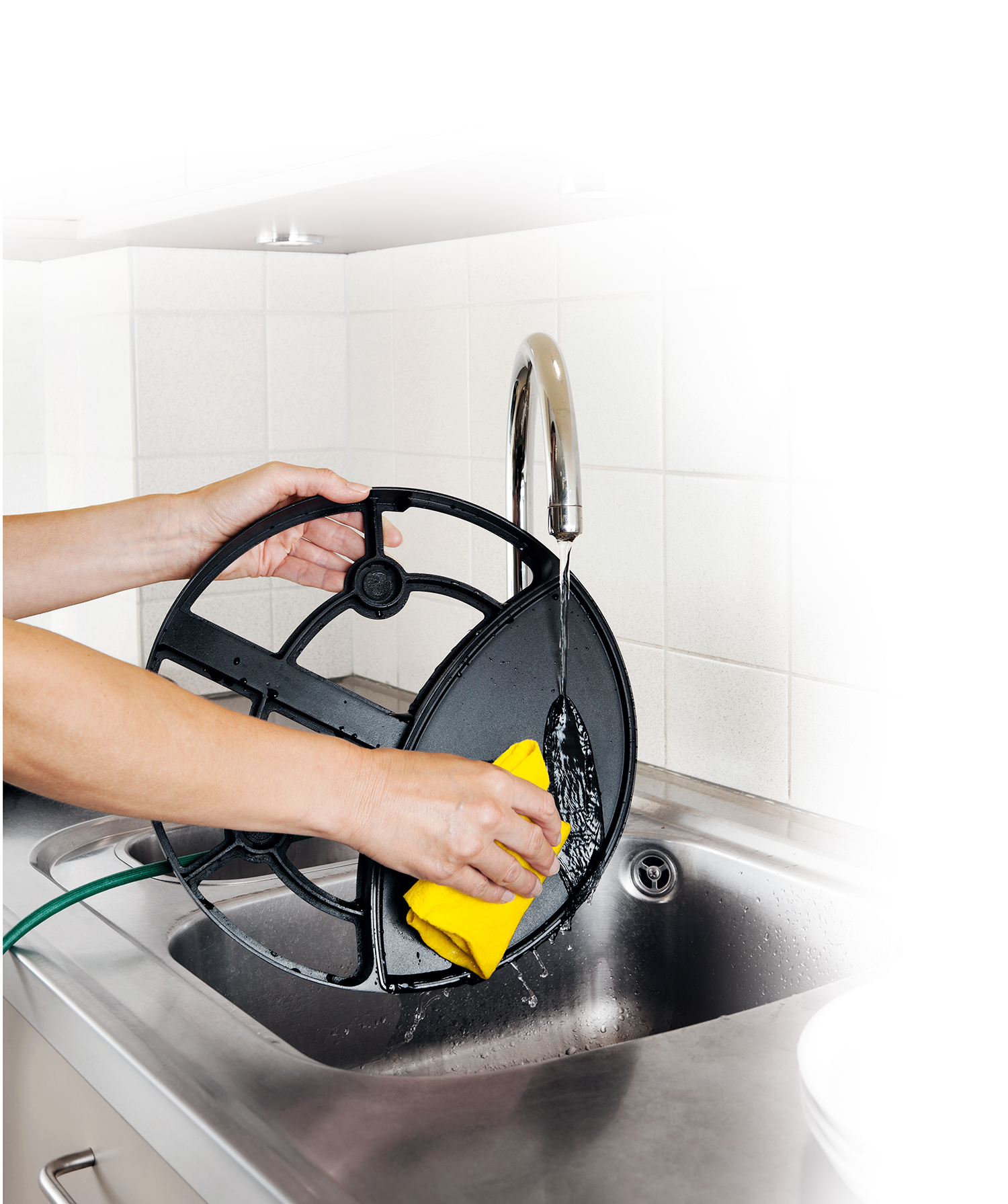 Handen die een zwart filter wassen in een roestvrijstalen spoelbak met een gele spons.