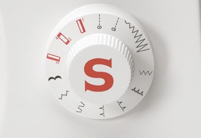 Dial de máquina de coser blanco con logo 'S' rojo y opciones de patrón de puntada. El dial está enfocado.