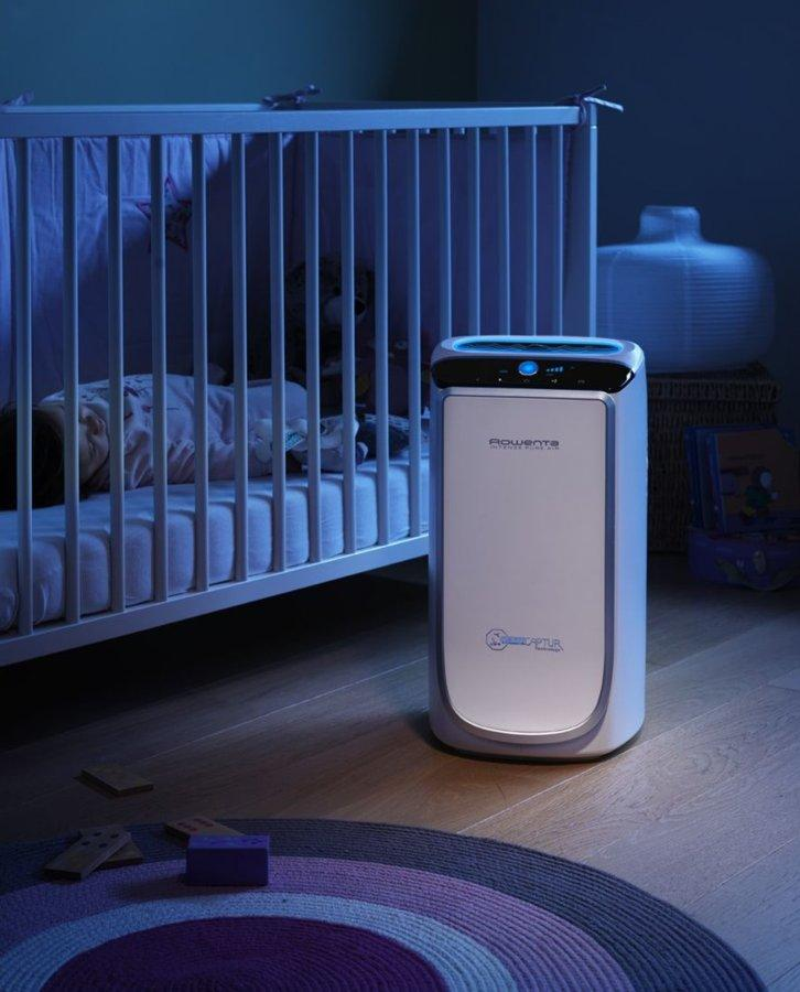 Una cuna con un purificador de aire blanco. La habitación tiene una alfombra y una luz nocturna.