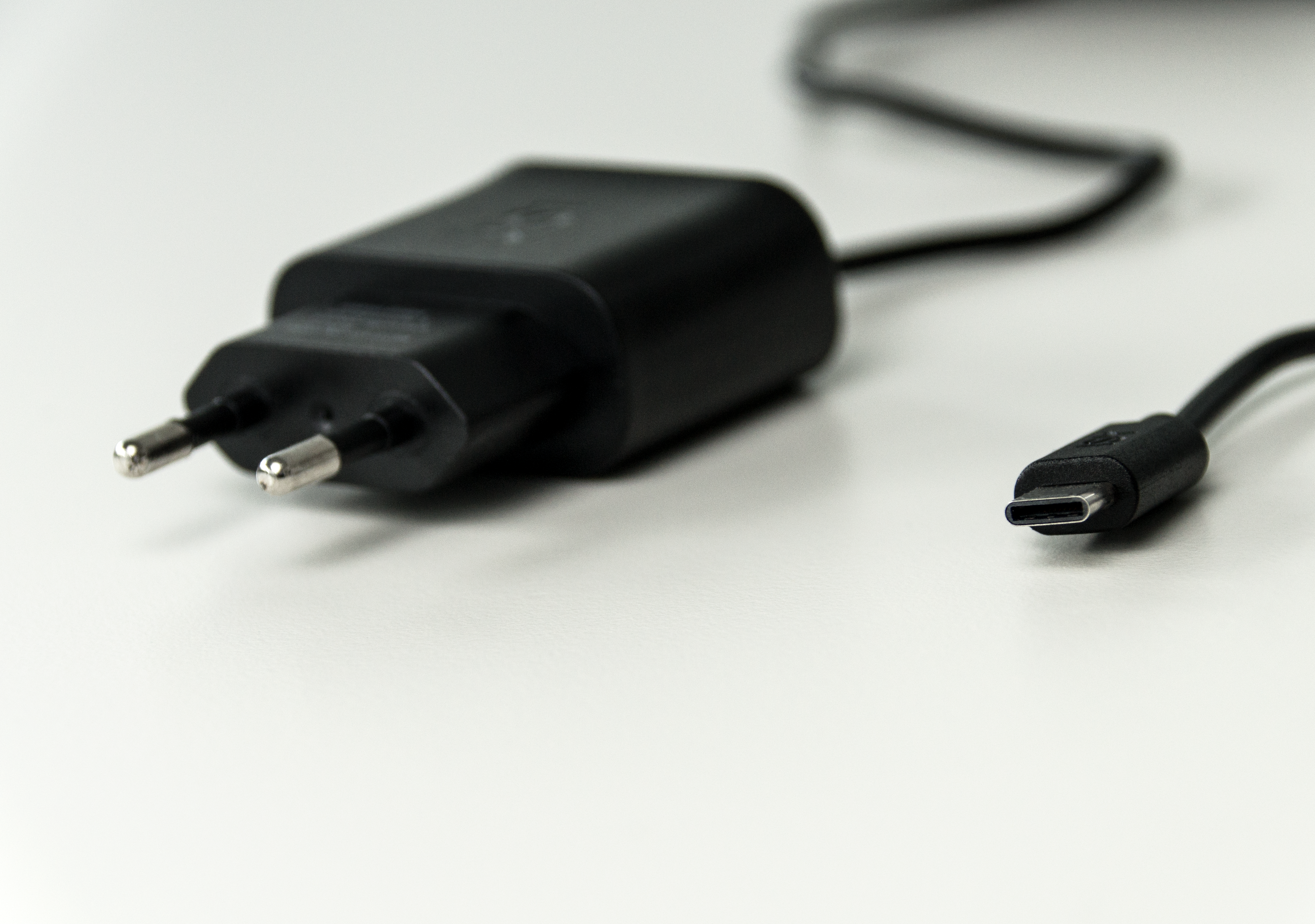 Schwarzes Telefonladegerät mit Stecker und USB-C-Anschluss auf weißer Oberfläche.