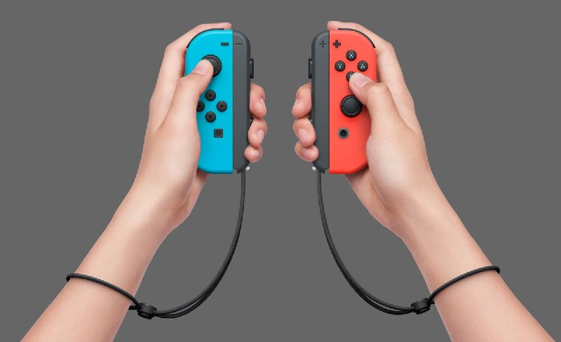 Dos manos sosteniendo Joy-Cons de Nintendo Switch azules y rojos, sobre fondo gris.