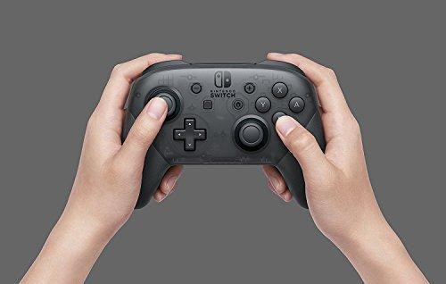 Manos sosteniendo un mando Pro de Nintendo Switch negro. Botones visibles, fondo gris.