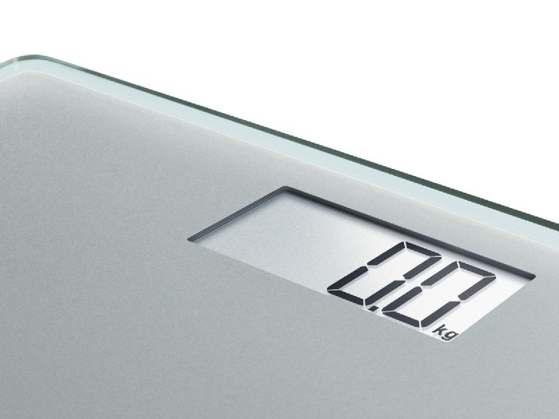 Báscula de baño digital. La pantalla muestra '0.0 kg'. Es plateada y blanca.
