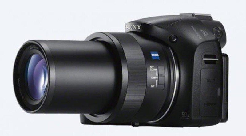 Cámara Sony negra con lente grande y anillo de zoom plateado sobre fondo blanco.