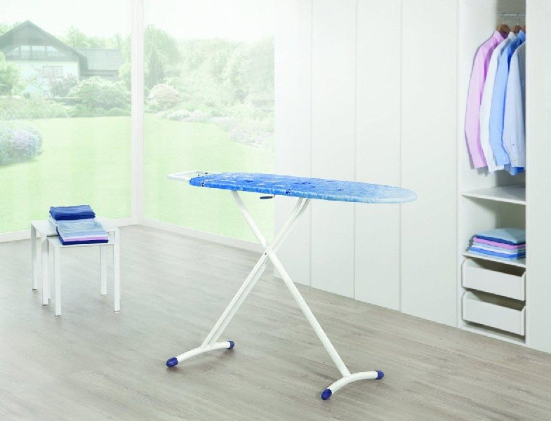 Tabla de planchar con estampado floral azul, marco blanco y una pequeña mesa con toallas dobladas.