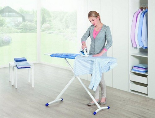 Mujer planchando una camisa a rayas en una tabla de planchar azul. Armario blanco detrás.