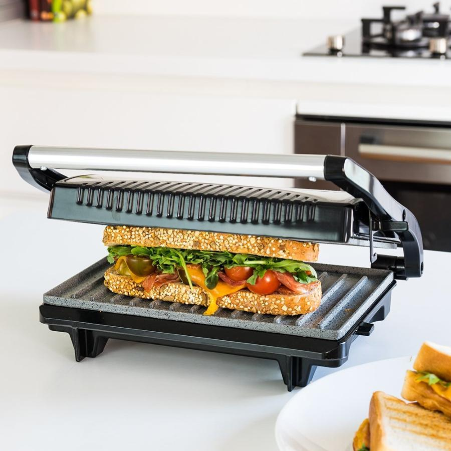 Prensa para sándwiches con un sándwich dentro. Tiene una parrilla negra y un asa de acero inoxidable. Sándwich en el mostrador.
