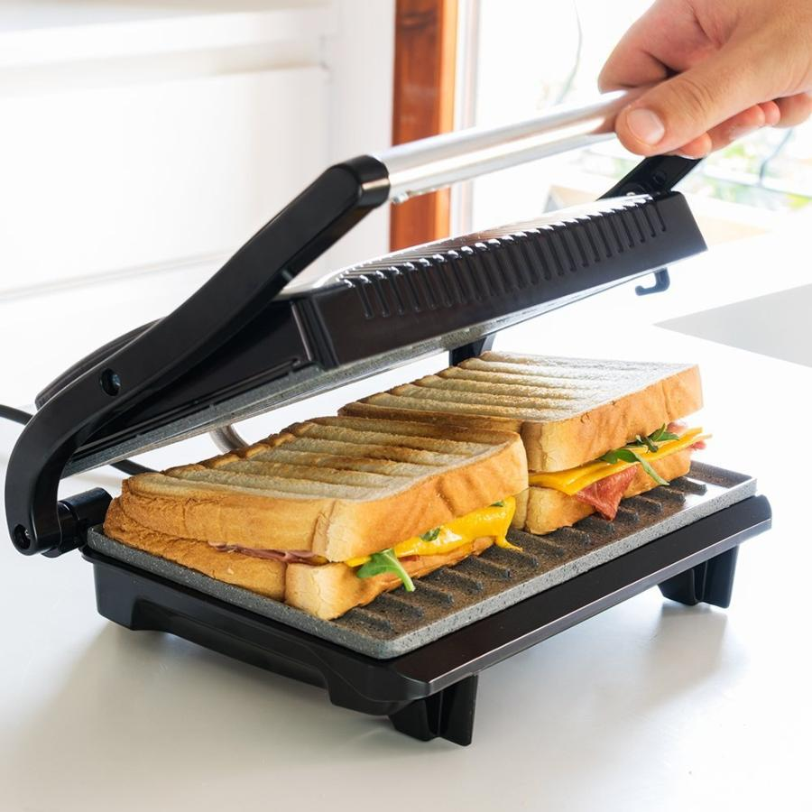 Sándwiches en una prensa panini negra. El sándwich tiene jamón, queso y rúcula.