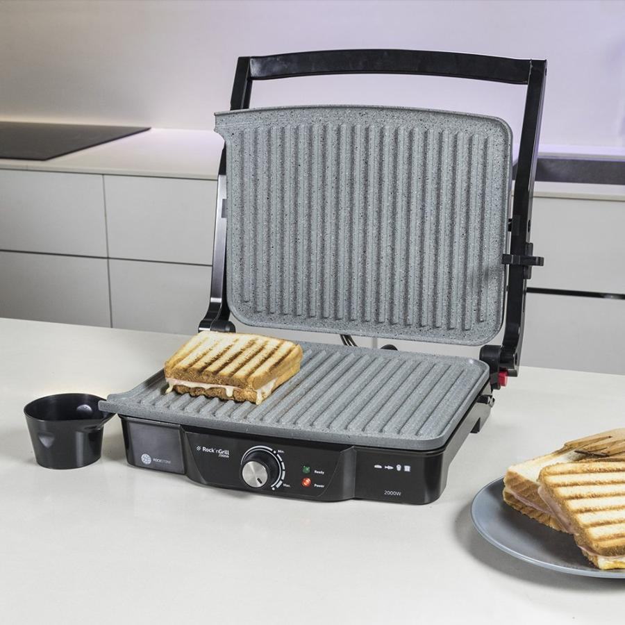 Grill panini abierto con sándwich tostado. Un cuenco negro y más sándwiches visibles.