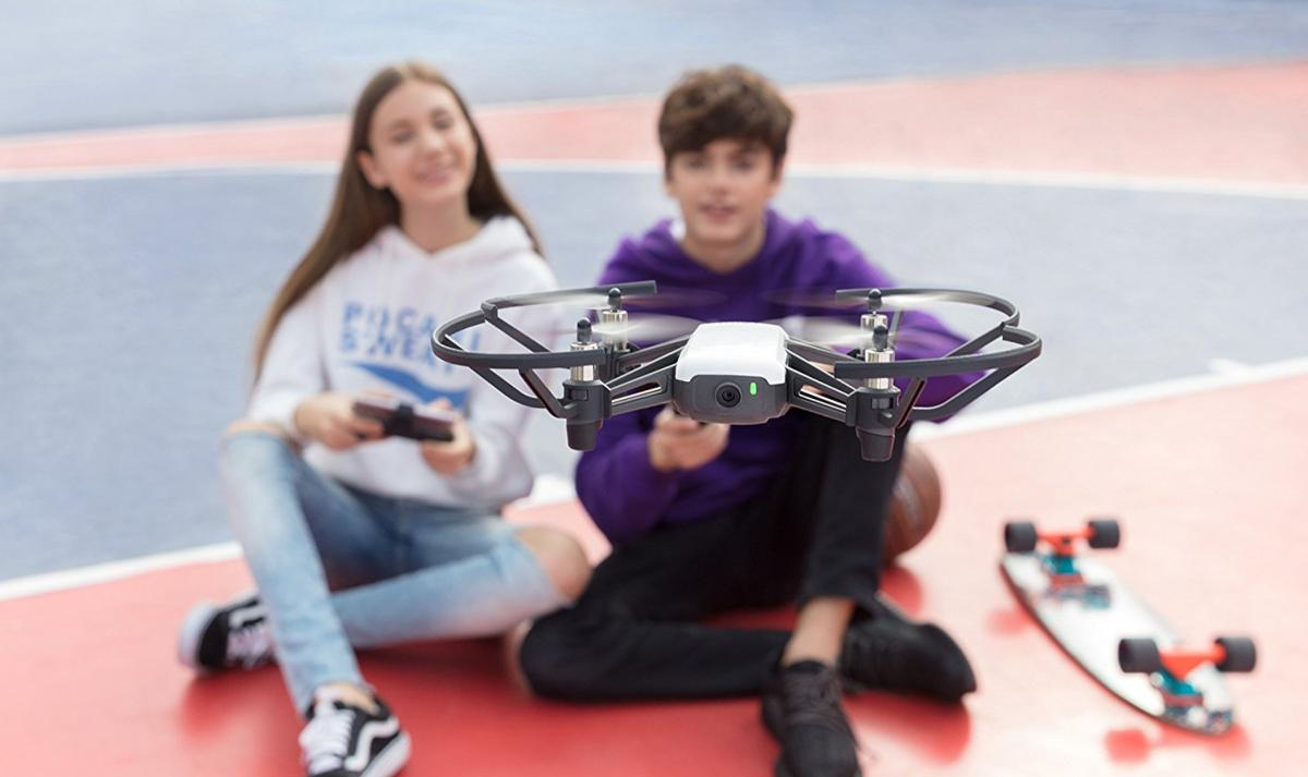 Dos niños jugando con un dron y una patineta en una cancha roja y azul.