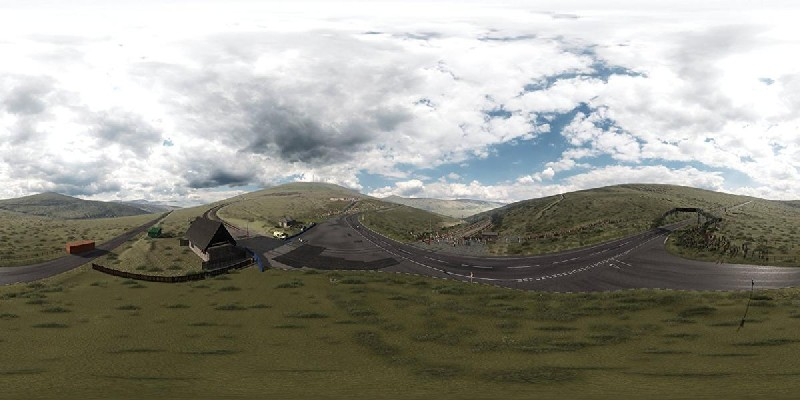 Vista panorámica de una carretera de montaña con un edificio a la izquierda y cielo nublado.