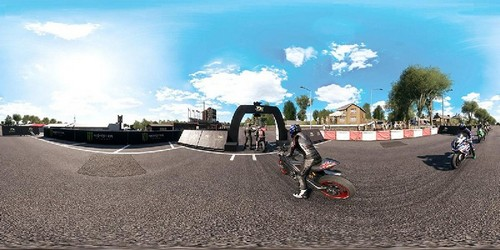 Carrera de motos en una pista. Pilotos, pancartas y espectadores son visibles.